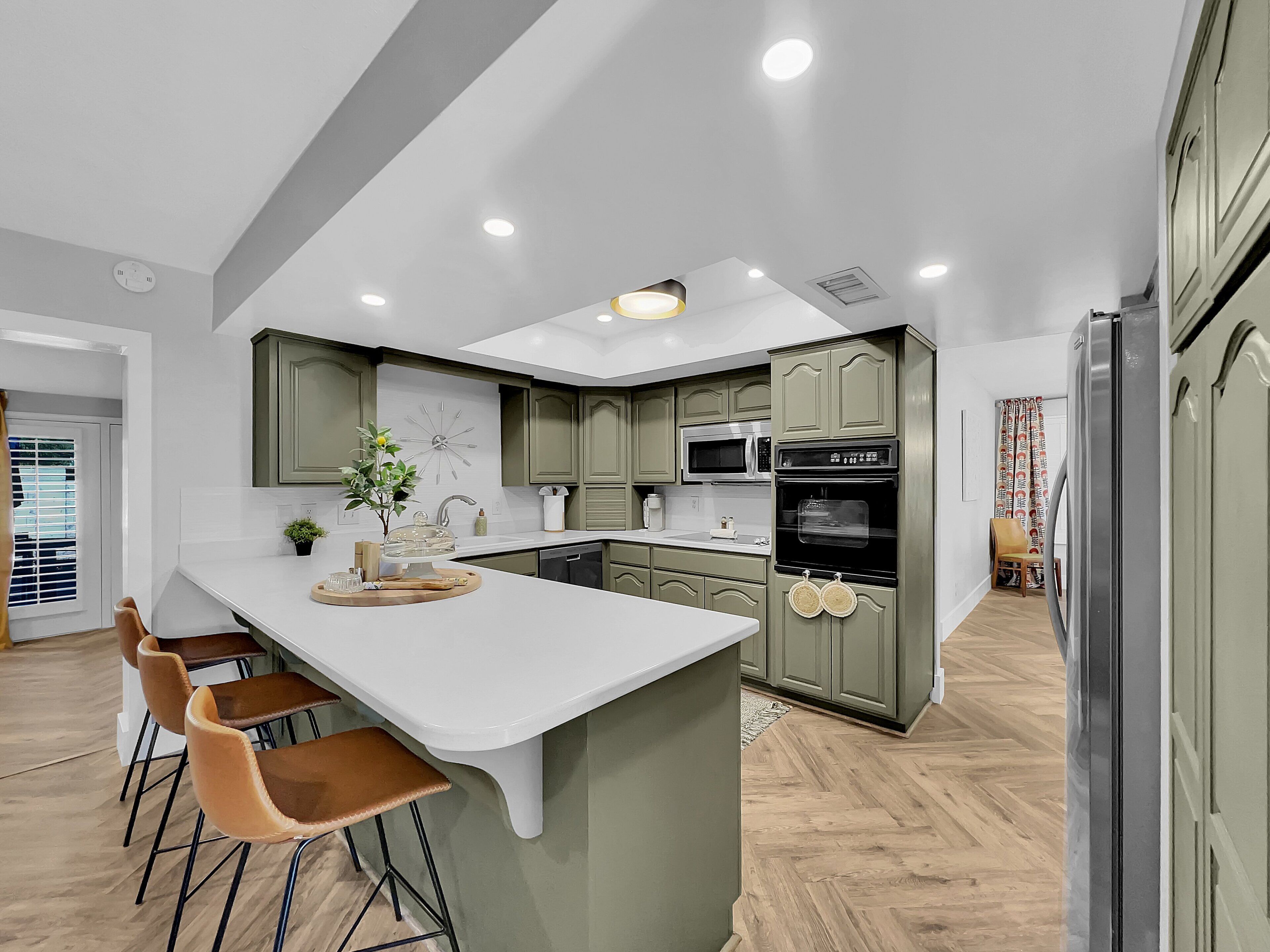 Cocina moderna con una isla central, armarios verdes, encimeras blancas y un microondas.