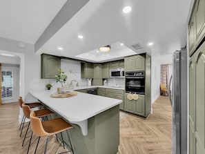 A modern kitchen with a central island, bar stools, green cabinets, a microwave, oven, and a refrigerator. - Los Lagos Mesa (Mesa)