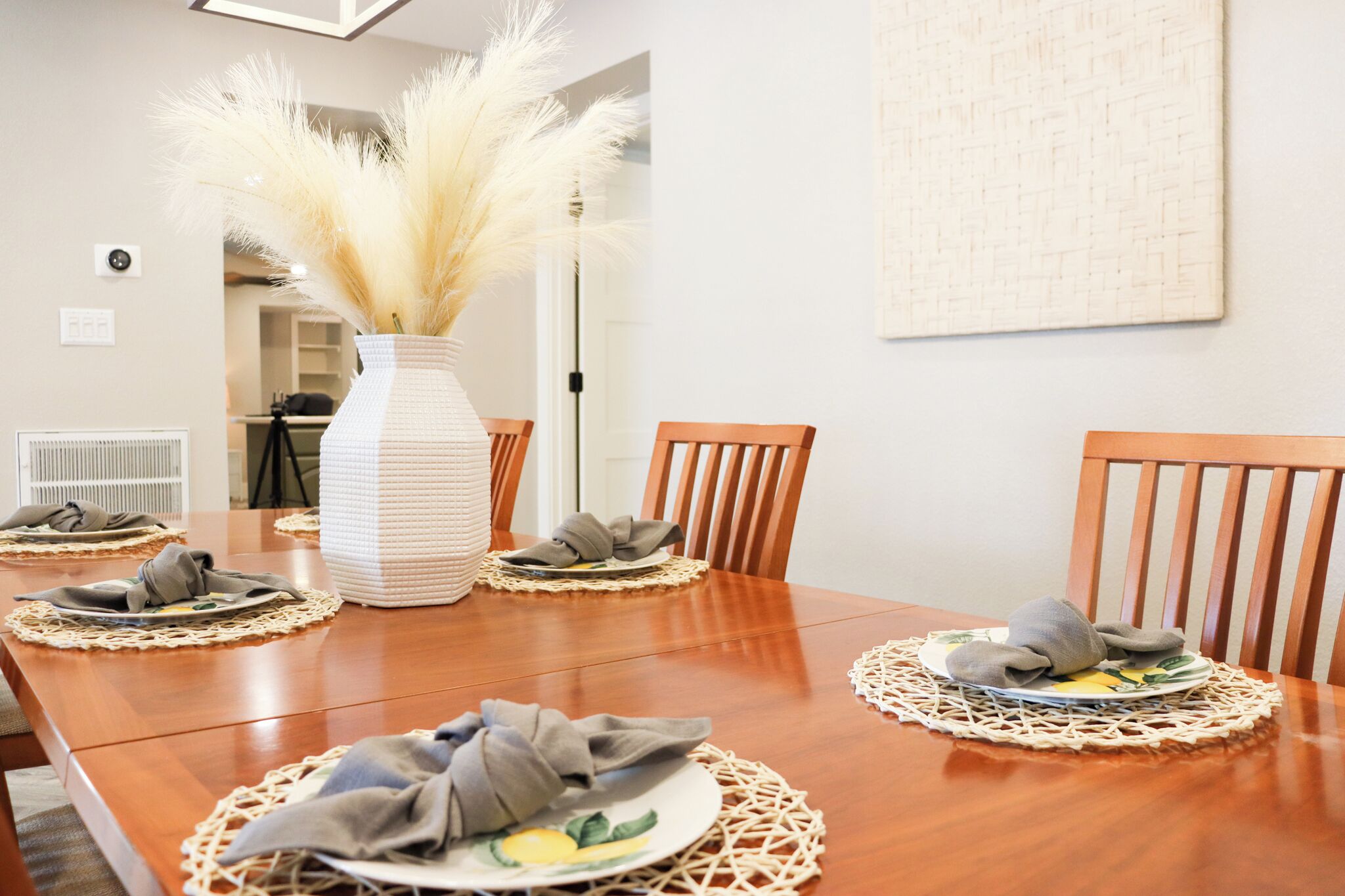 A dining table set with plates, napkins, and a vase of pampas grass.