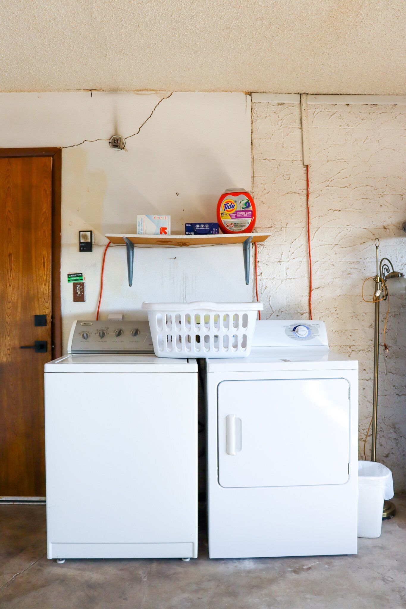 A laundry area with two white washing machines, a shelf with laundry supplies, and a wooden door.