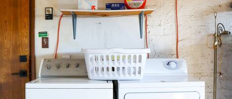 A laundry area with two white washing machines, a shelf with laundry supplies, and a wooden door.
