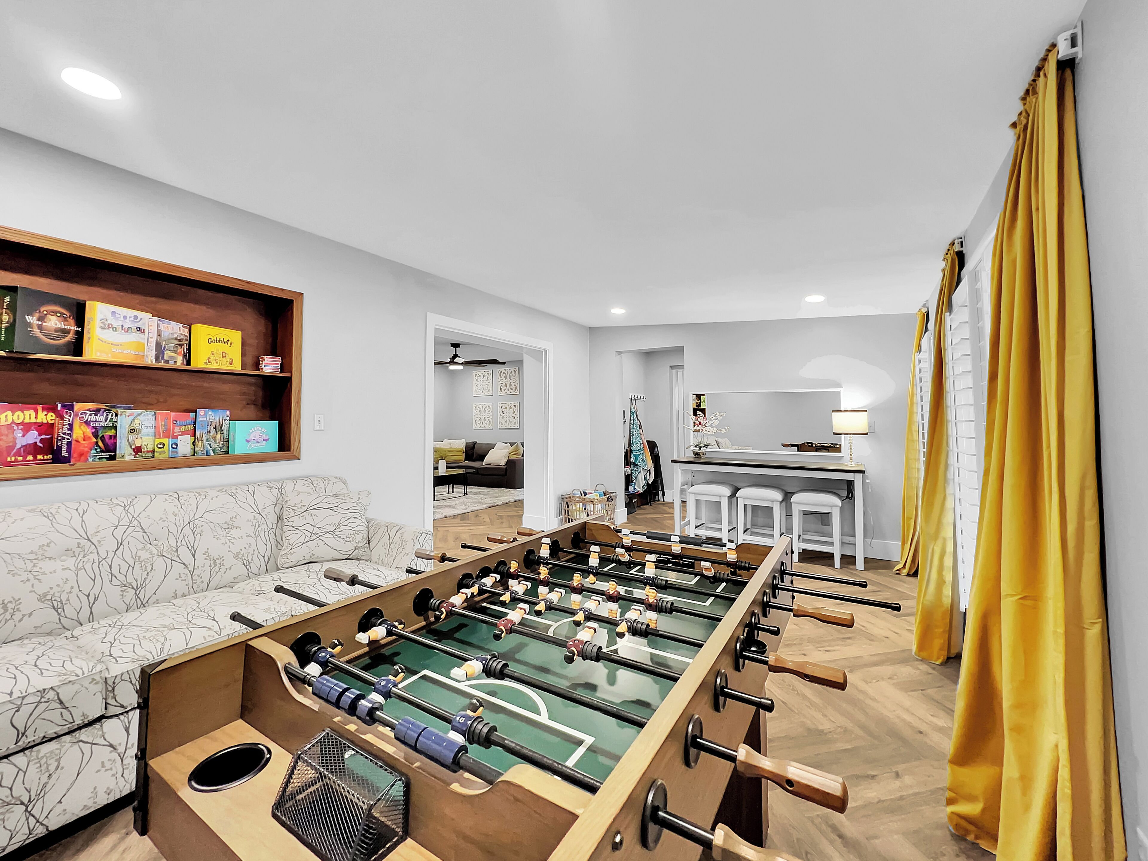 Un salon moderne avec un baby-foot, un canapé et un coin cuisine à l’arrière-plan.