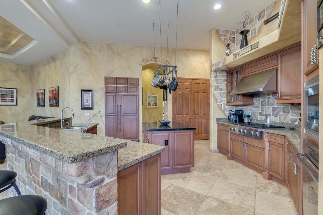 A spacious kitchen with granite countertops, wooden cabinets, and a stone accent wall.