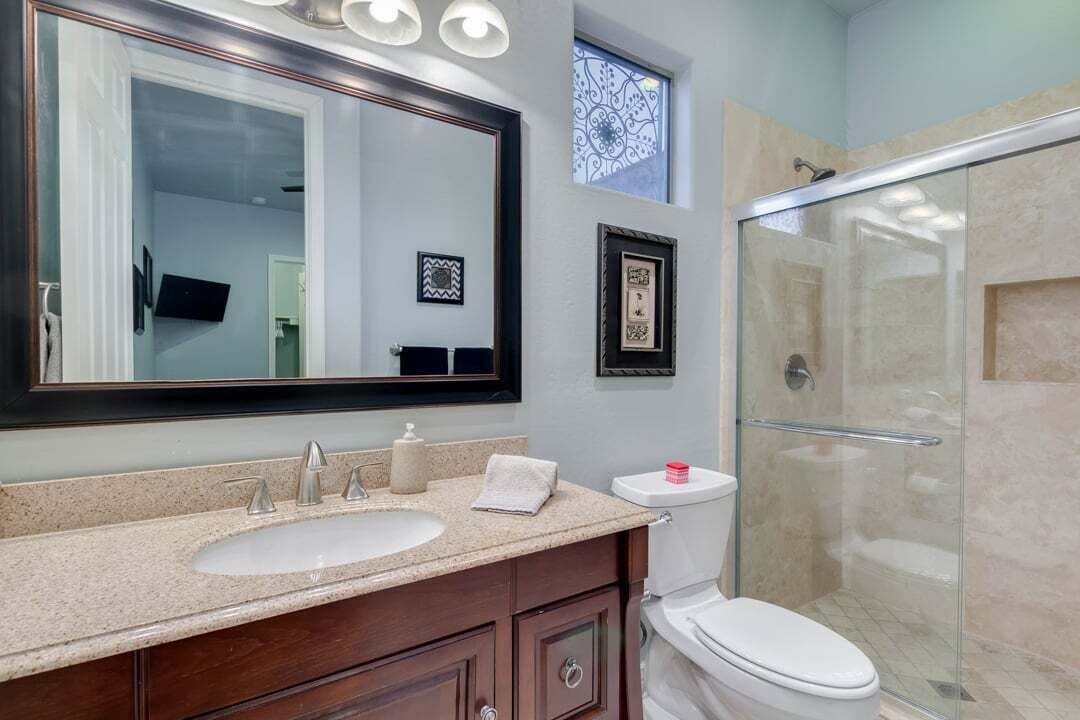 A bathroom with a large mirror, two sinks, a toilet, and a glass-enclosed shower.