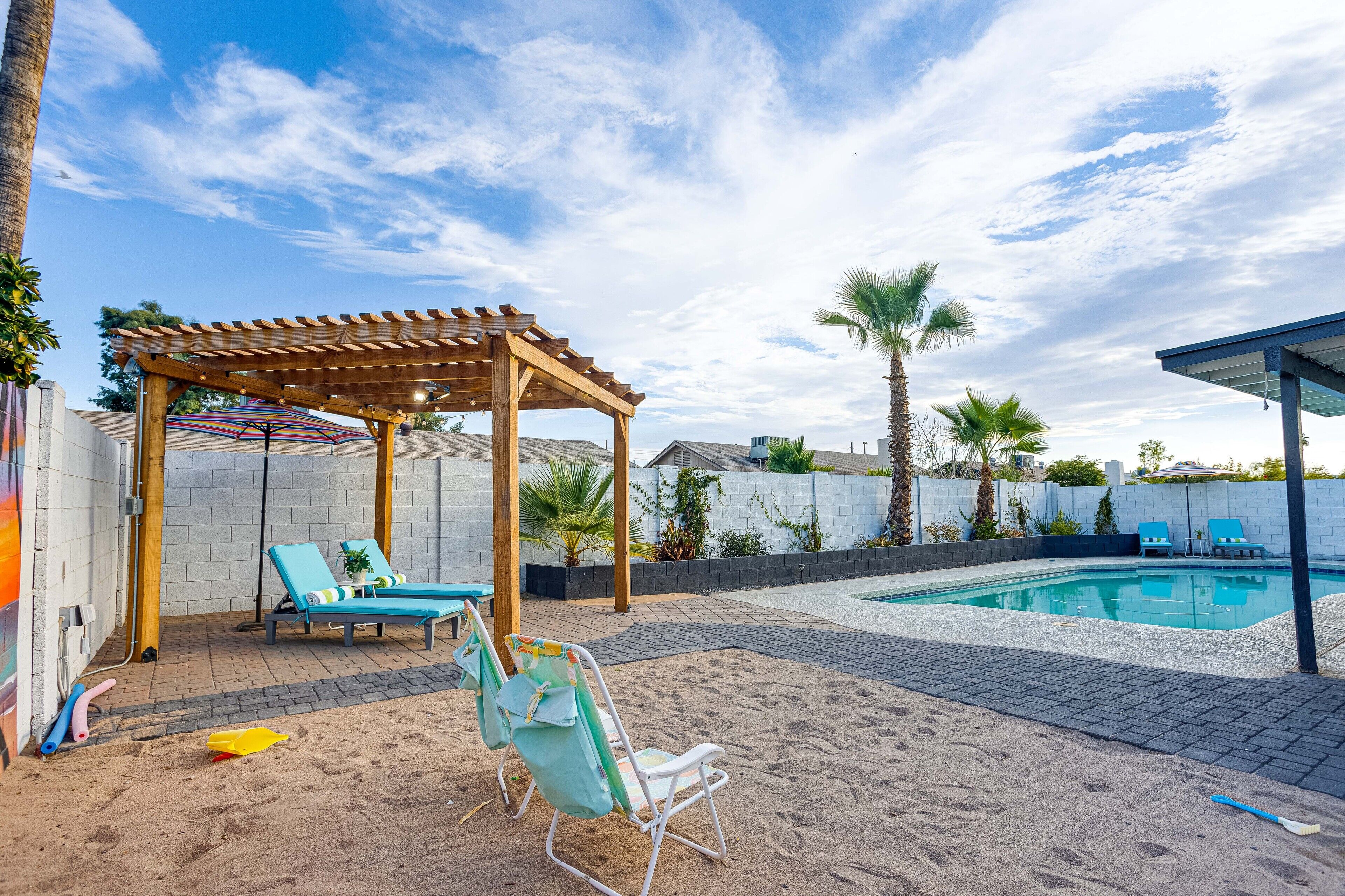 En baghave med pool, liggestole, pergola og et sandareal.
