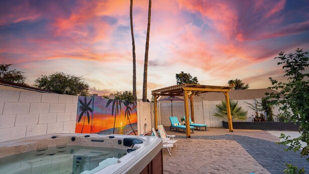 Un bain à remous, des chaises longues et une fresque représentant un coucher de soleil, le tout dans un cadre de jardin.