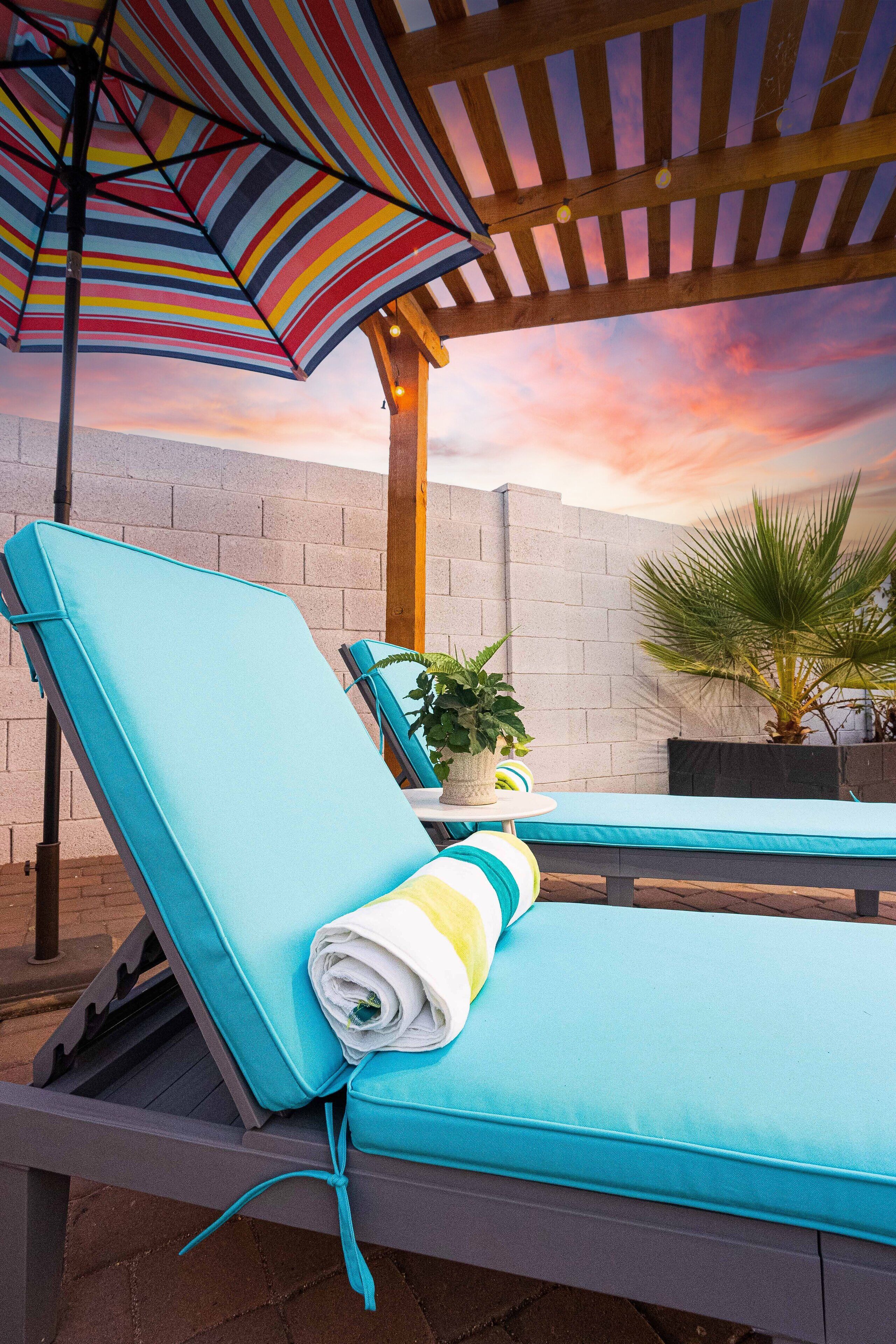 Zona de piscina con sillas de descanso, una sombrilla a rayas y vista al atardecer.