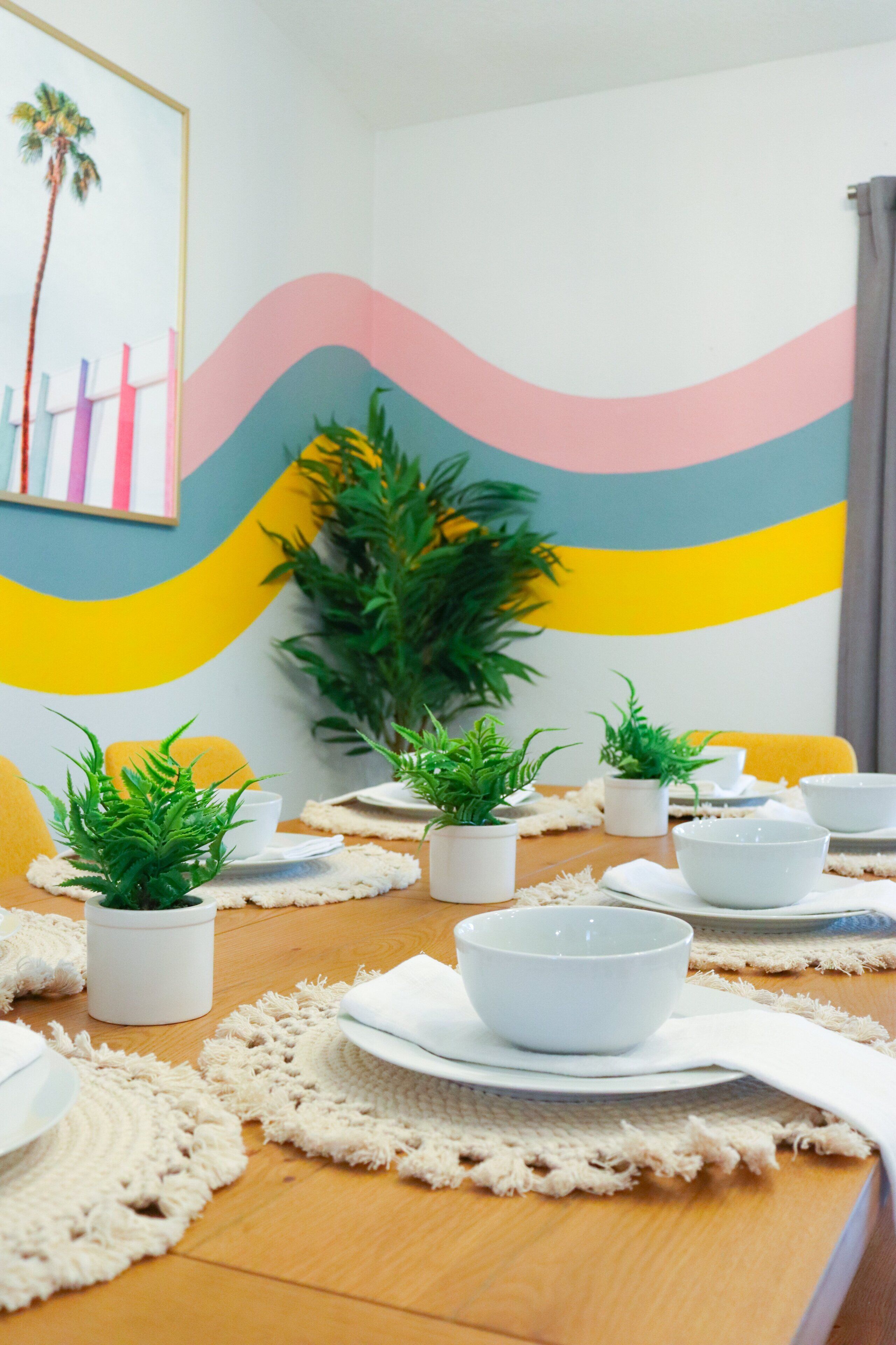 A dining area with a wooden table set for a meal, surrounded by potted plants and white bowls.