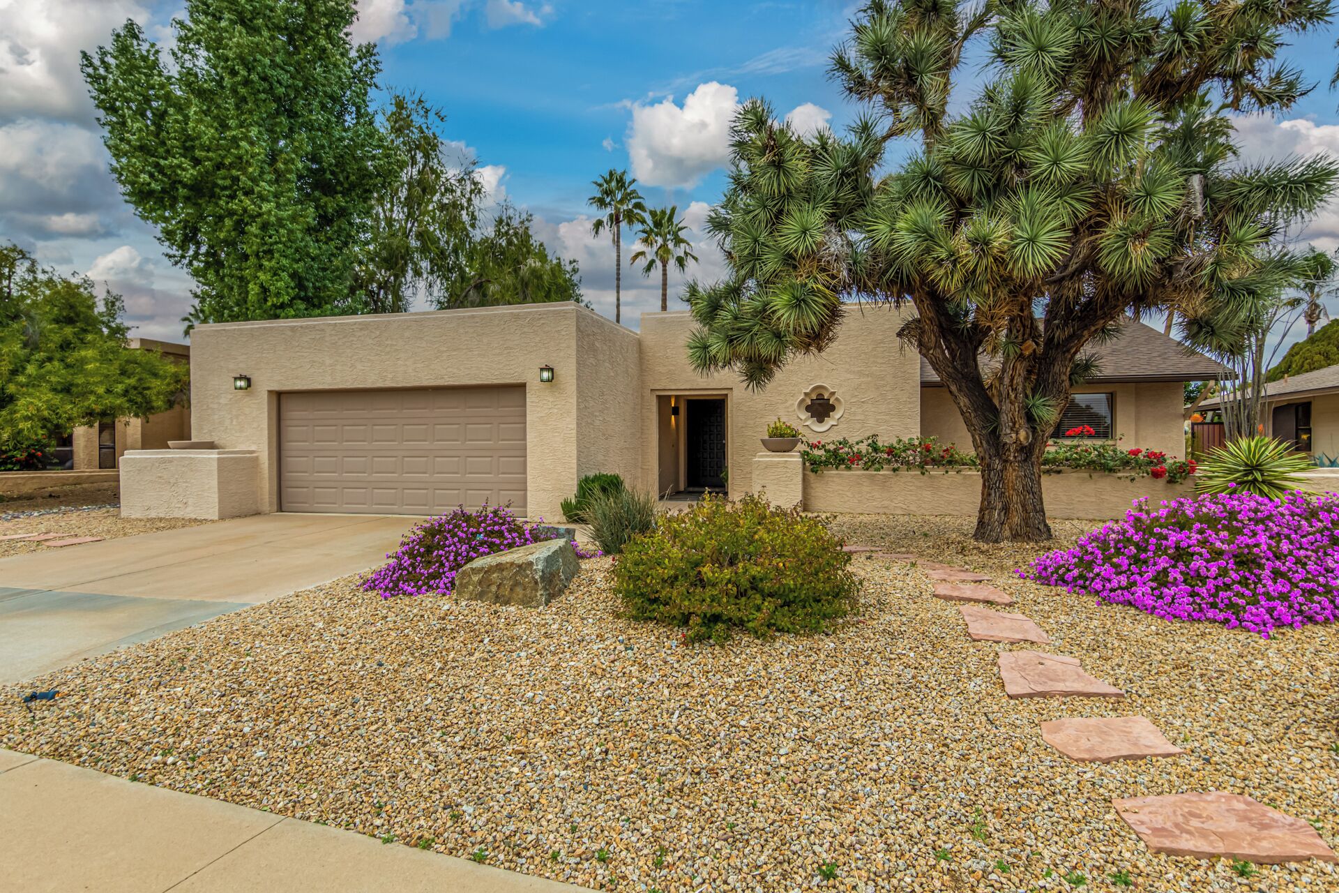 A modern house with a garage, surrounded by a gravel driveway and various plants.