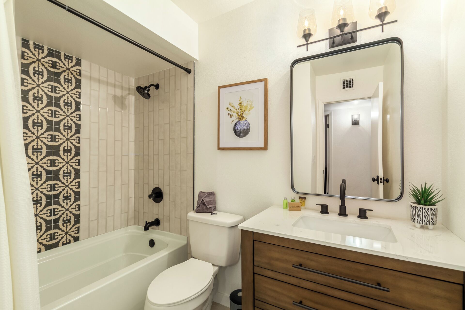 Une salle de bain avec une baignoire, des toilettes, un meuble-lavabo avec un miroir et un tableau encadré au mur.