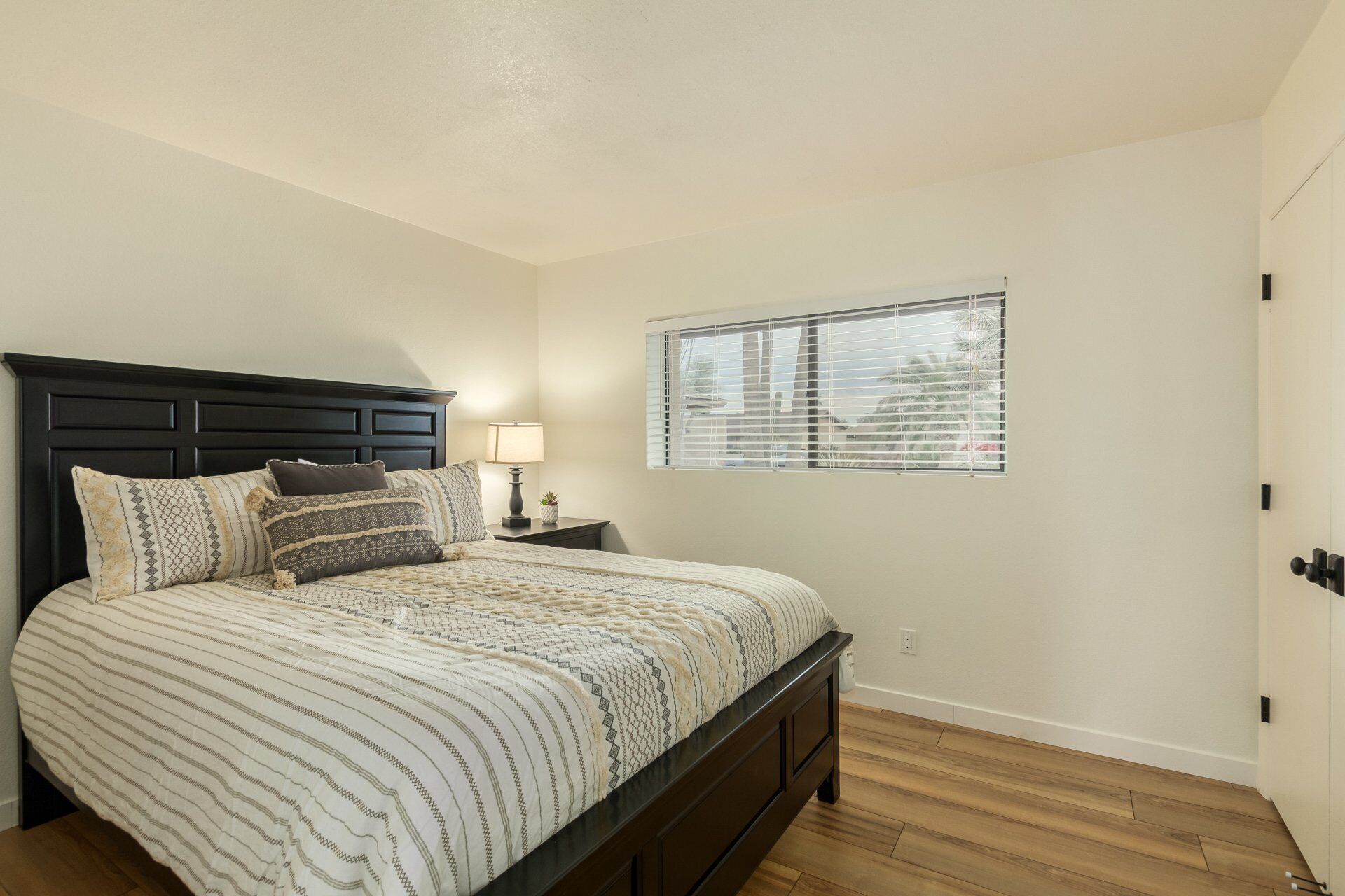 A bedroom with a bed, a nightstand, a lamp, and a window with blinds.
