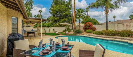 A backyard with a swimming pool, outdoor furniture, and a barbecue grill.