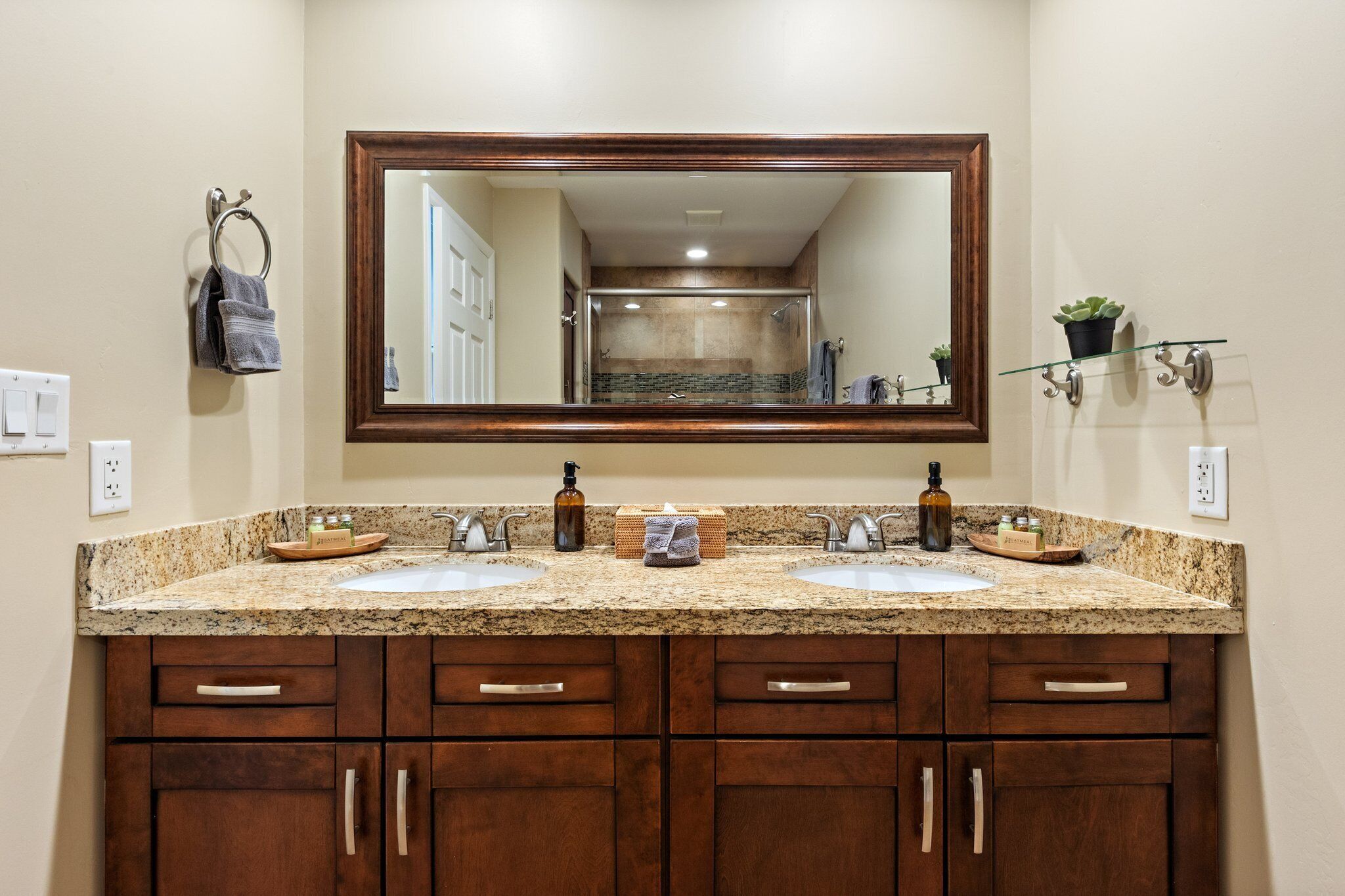 A bathroom with a large mirror, two sinks, wooden cabinets, and a countertop with toiletries.