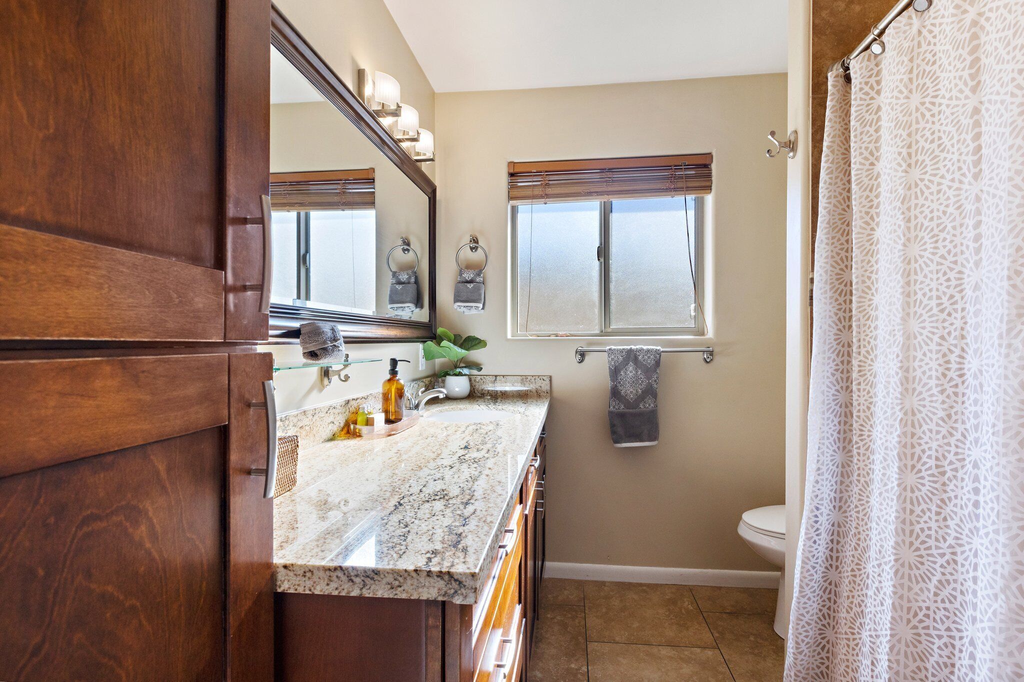 A bathroom with a marble countertop, wooden cabinets, a toilet, and a shower curtain.