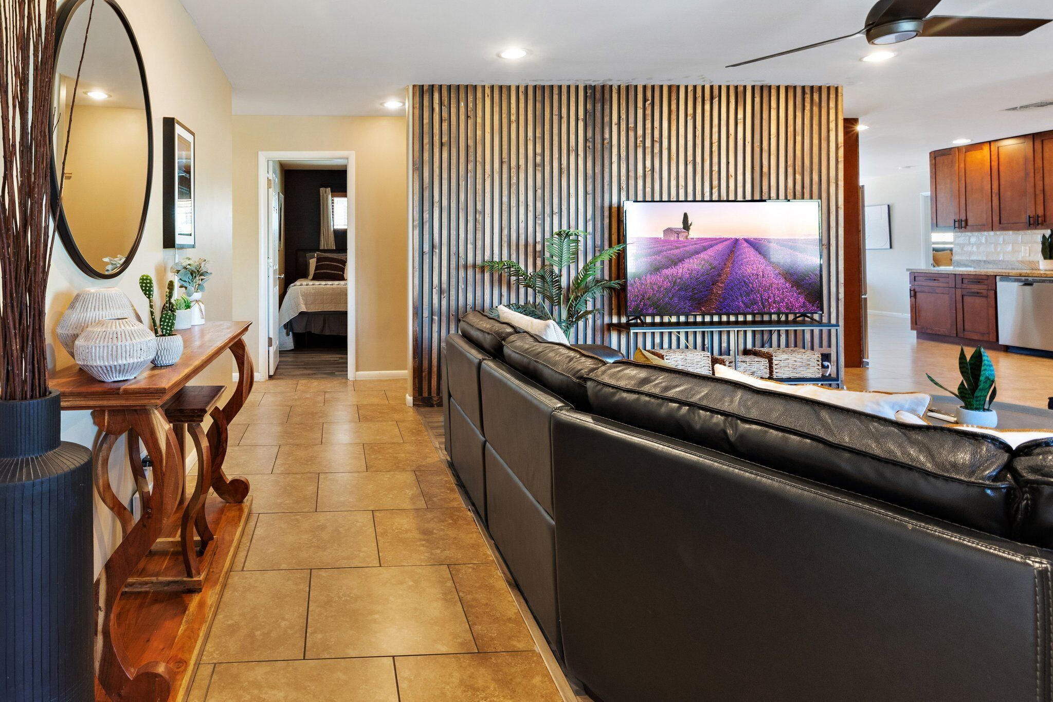 A modern living room with a leather sofa, a TV mounted on a wooden wall, a dining area with a wooden table, and a kitchen area.