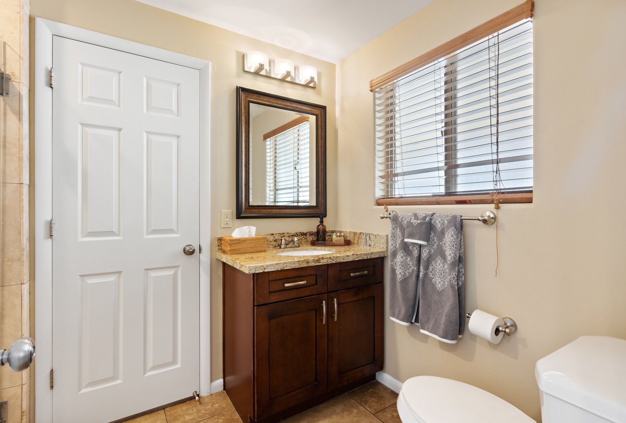A bathroom with a white door, a sink with a mirror above it, a towel rack with a towel, and a toilet.
