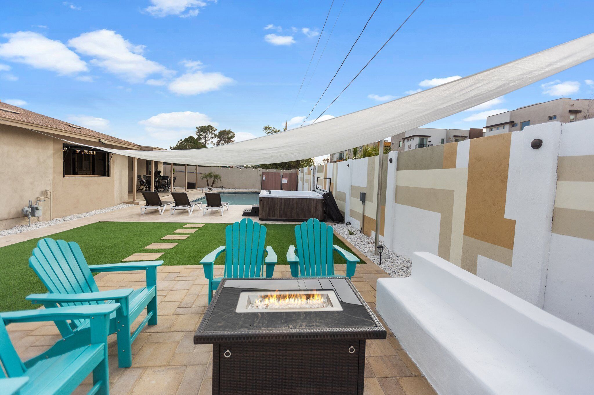 Un espace extérieur aménagé en terrasse, avec un foyer, des chaises vertes et une piscine.