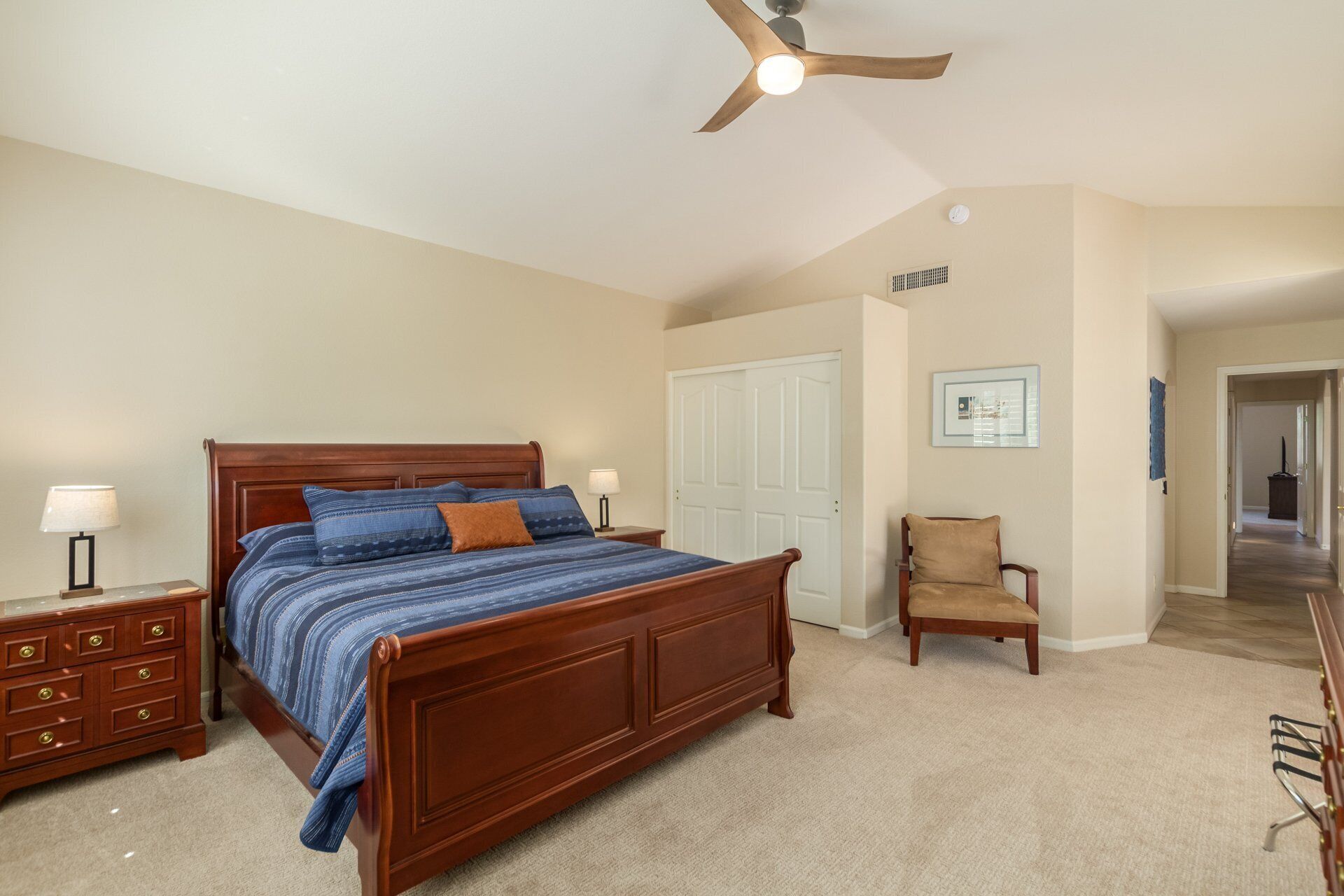 A bedroom with a wooden bed, a nightstand, a chair, and a ceiling fan.