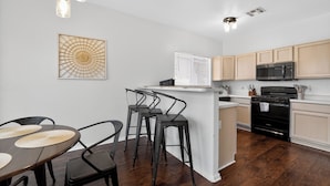 A modern kitchen with a dining area, wooden cabinets, a microwave, and a stove. - Sonesta Tucson (Tucson)