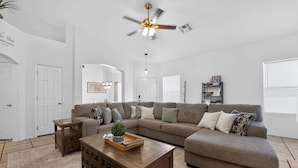 A living room with a sectional sofa, a wooden coffee table, a ceiling fan, and a bookshelf. - Sonesta Tucson (Tucson)