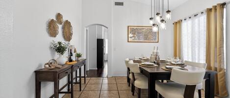 A dining area with a long table, chairs, hanging lights, and wall decor.