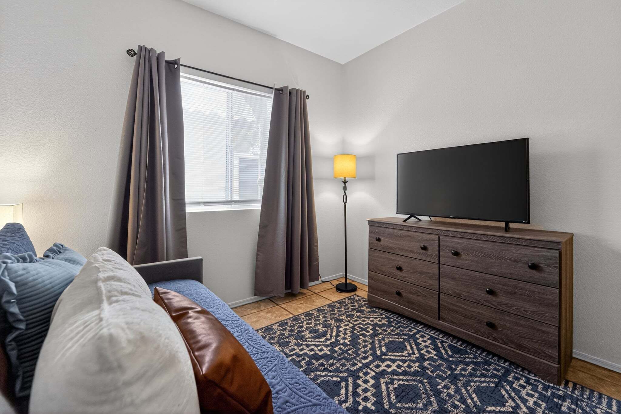 A bedroom with a bed, a TV, a dresser, and a window with curtains.
