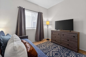 Une chambre à coucher avec un lit, une télévision, une commode et une fenêtre avec des rideaux.