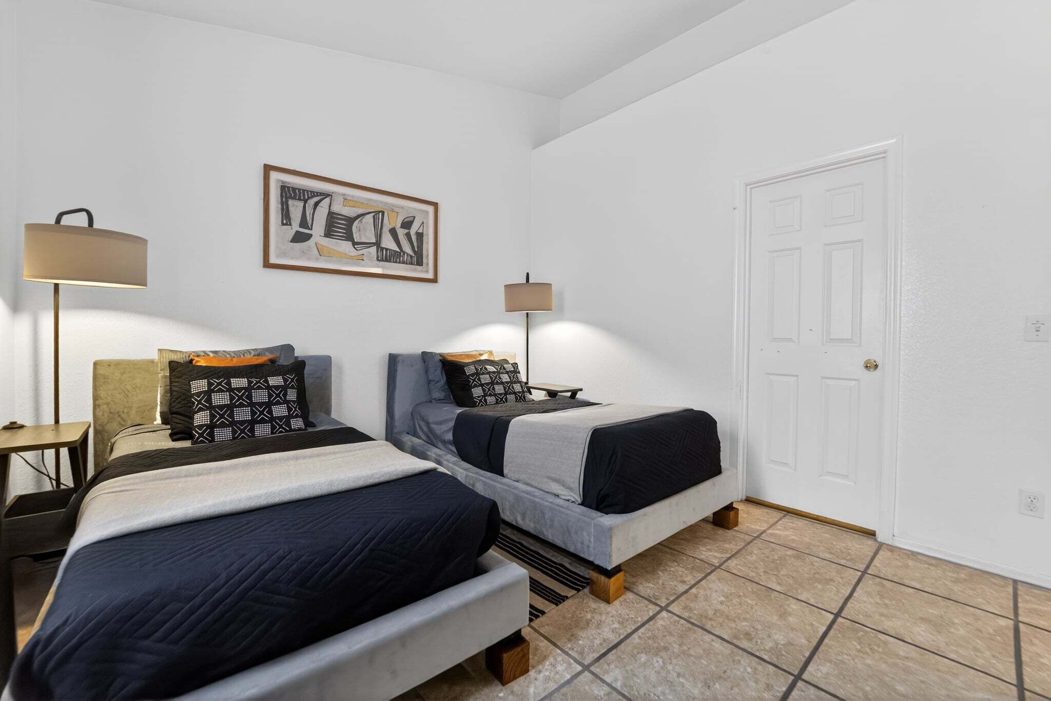 Een slaapkamer met twee bedden, een deur, een lijst met een afbeelding en een lamp.
