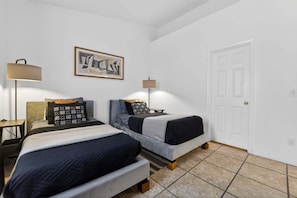 Une chambre avec deux lits, une porte, un tableau encadré et une lampe.
