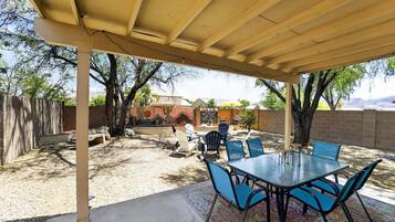 A covered patio with a table and chairs, a concrete floor, and a view of a house and trees in the background.