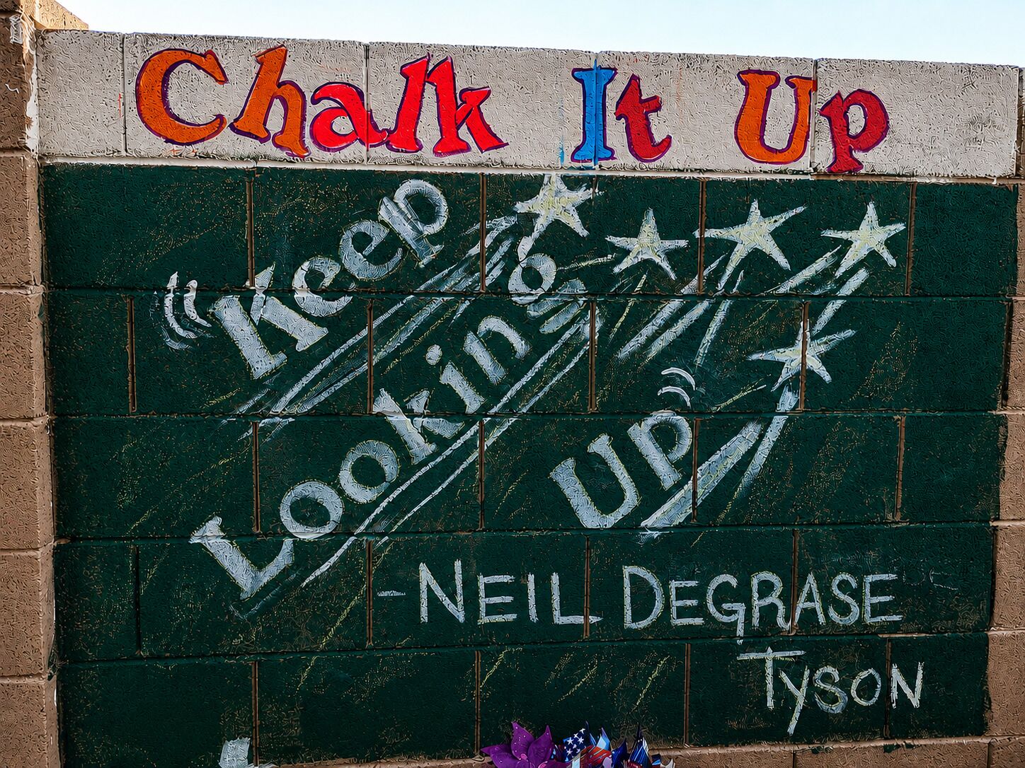 Un tableau noir orné de phrases motivantes et d’un nom, Neil DeGrasse Tyson, ce qui indique qu’il s’agit d’un élément permanent à vocation éducative ou inspirante.