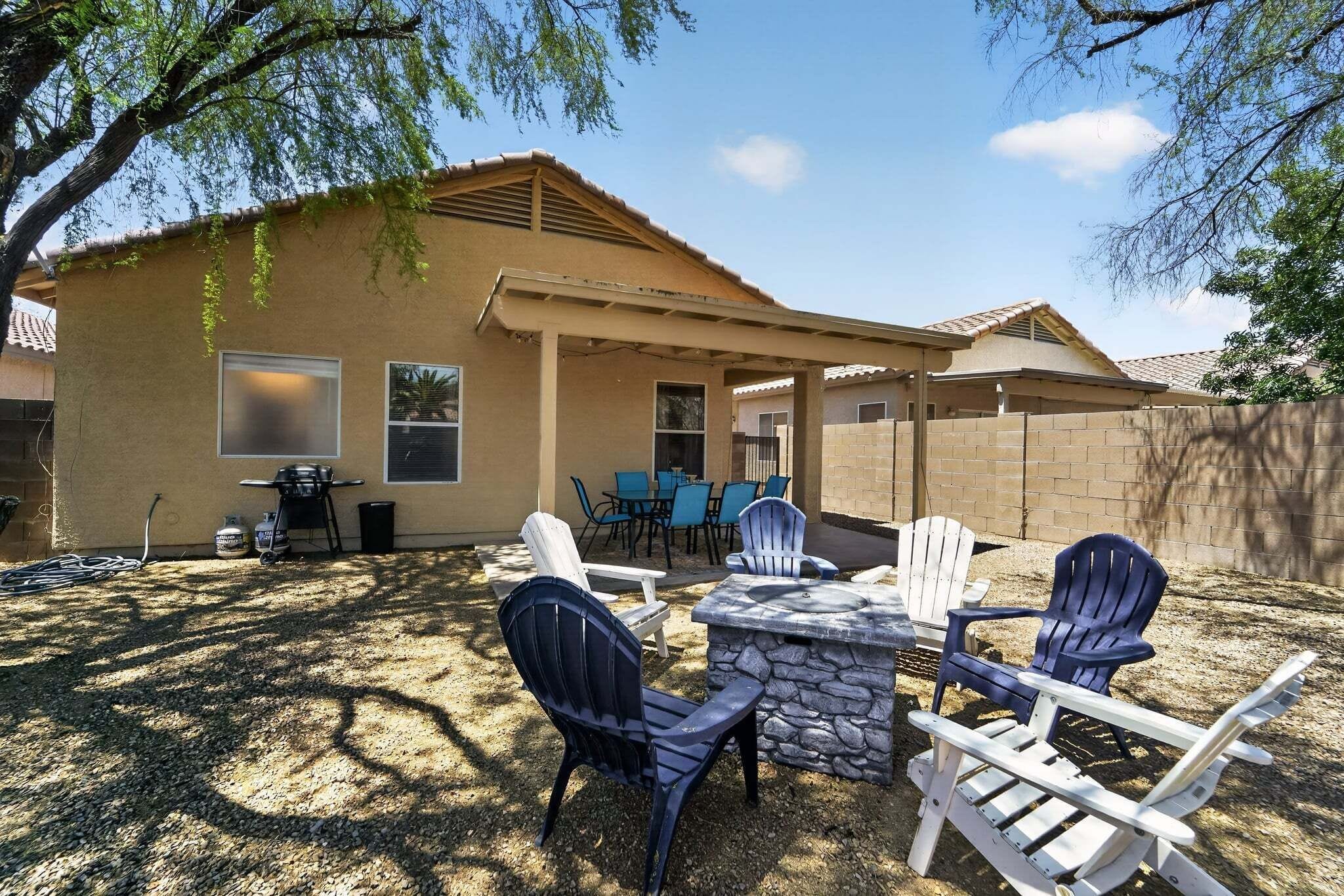 A patio area with Adirondack chairs, a stone table, and a barbecue grill.