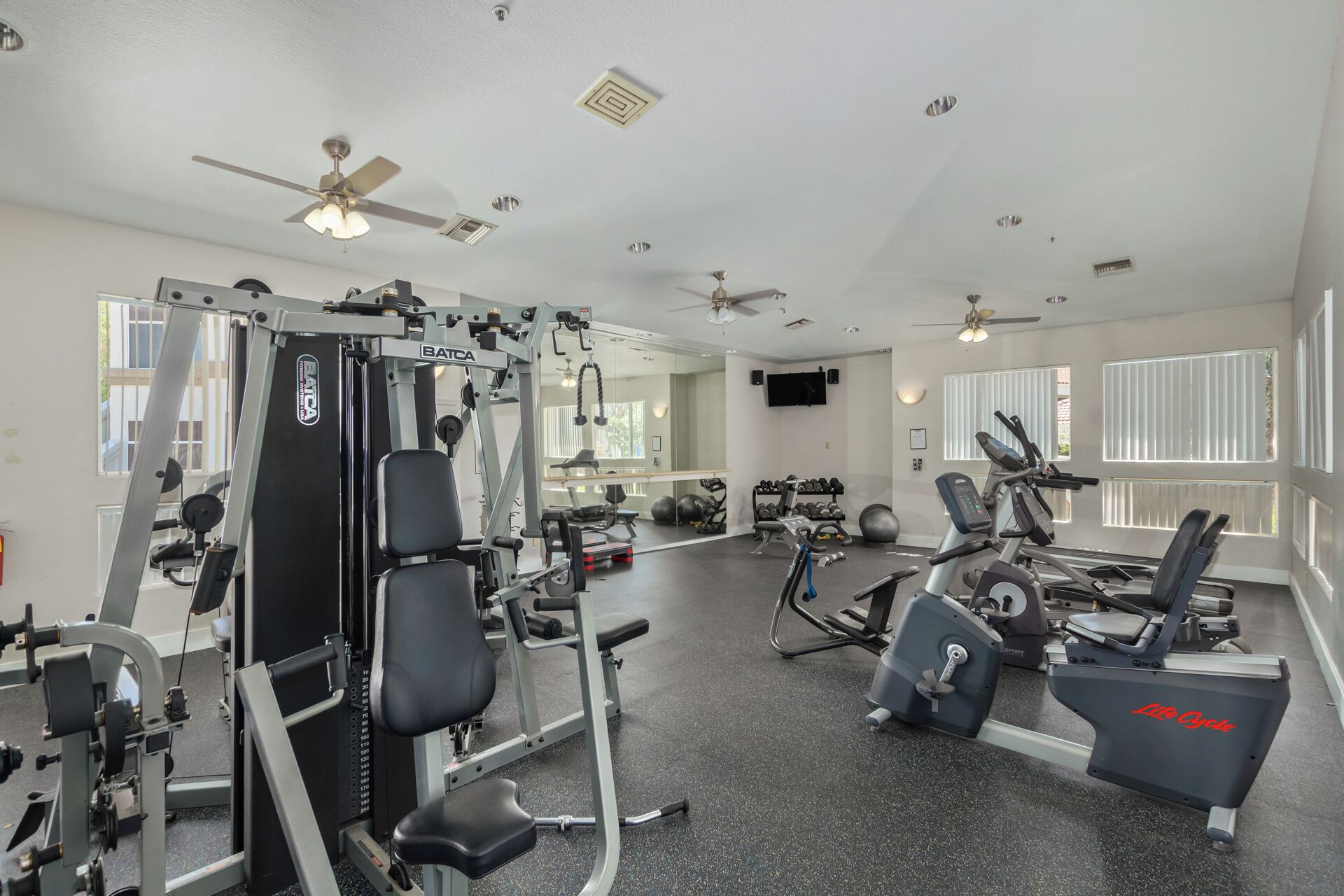 A gym with various exercise equipment, including a weight machine, treadmills, and dumbbells.