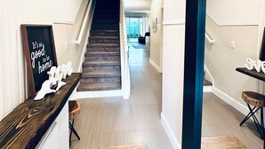 Un pasillo moderno con una escalera de madera, un banco y vista al área de estar.