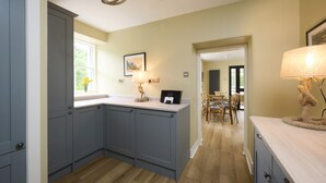 A kitchen with grey cabinets, a window with flowers, a dining area with chairs, and a lamp.