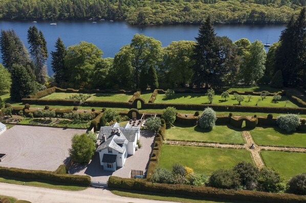 A large estate with a well-maintained lawn, a formal garden, and a lake in the background.