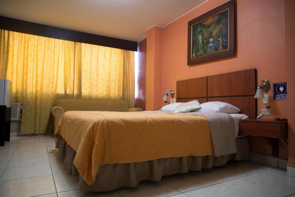 Ein Hotelzimmer mit Bett, Schreibtisch, Stuhl, einem Bild an der Wand und einem Fenster mit Vorhängen.