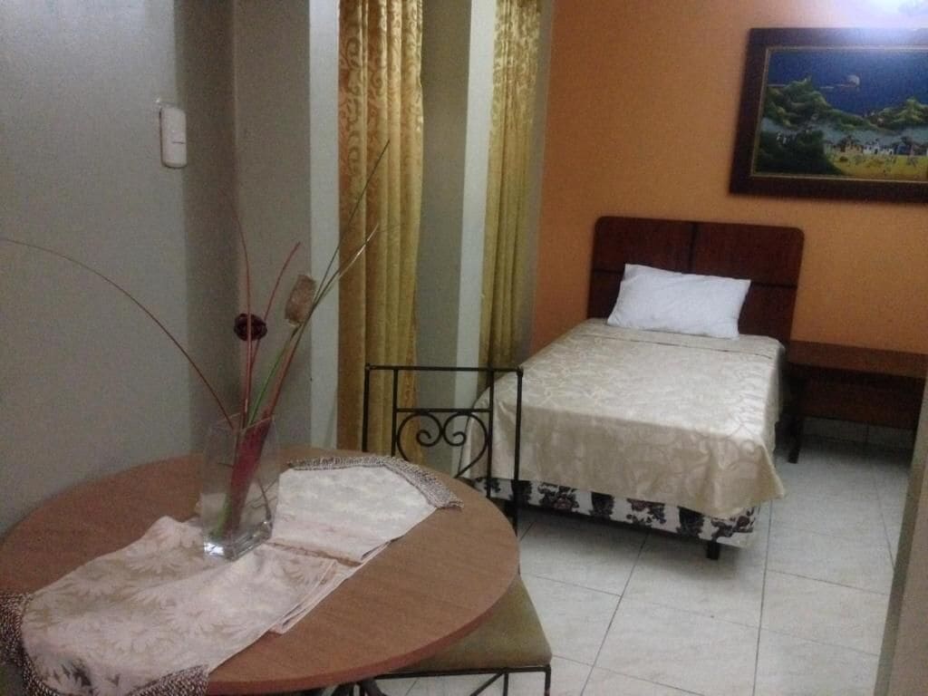 A hotel room with a bed, a round table with a vase, and curtains.