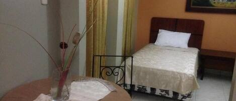 A hotel room with a bed, a round table with a vase, and curtains.