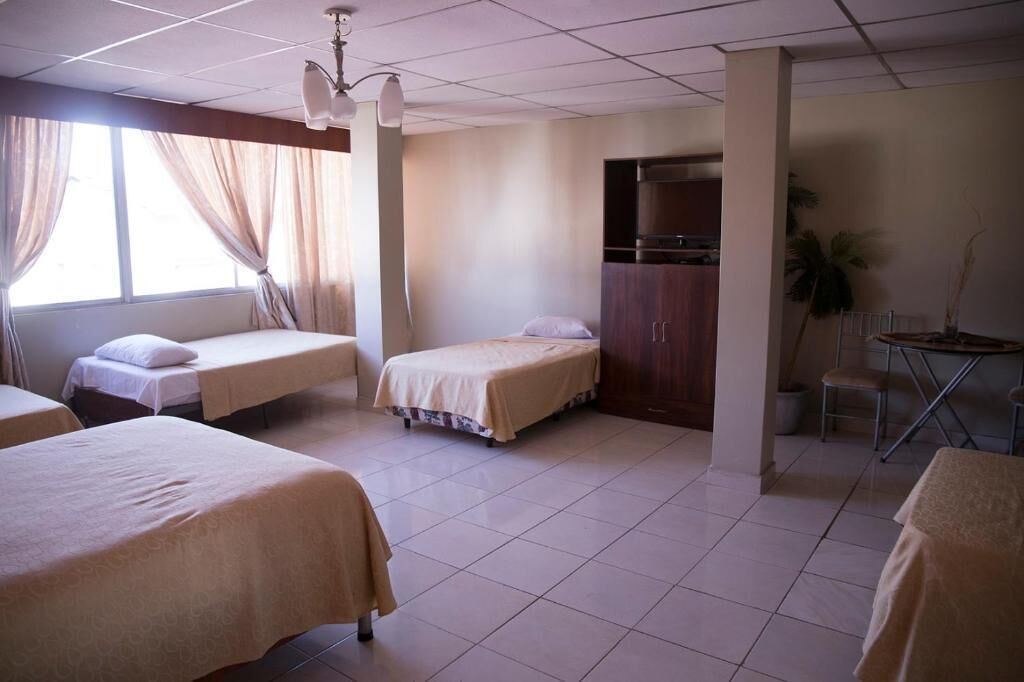 A hotel room with three single beds, a desk, and a chair.
