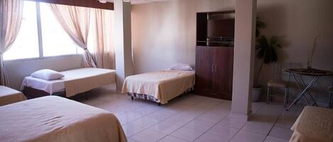 A hotel room with three single beds, a desk, and a chair.