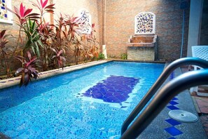 A swimming pool with mosaic tiles, surrounded by plants and a brick wall with decorative windows. - Tropical Inn (Guayaquil)
