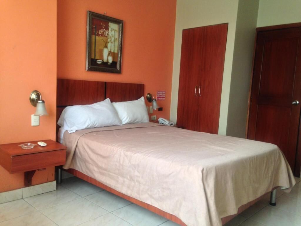 A hotel room with a bed, a nightstand, a telephone, and a door.