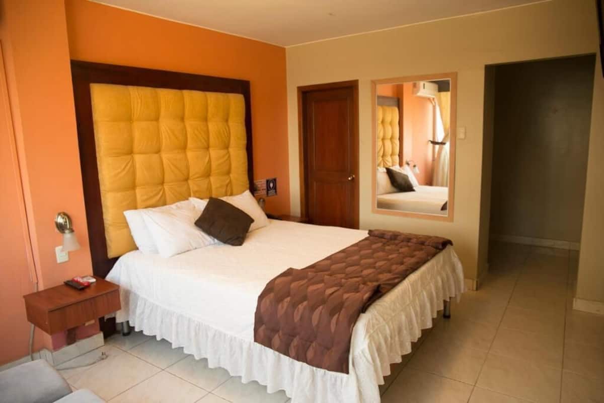 A hotel room with a large bed, a bedside table, a nightstand, and a mirror on the wall.