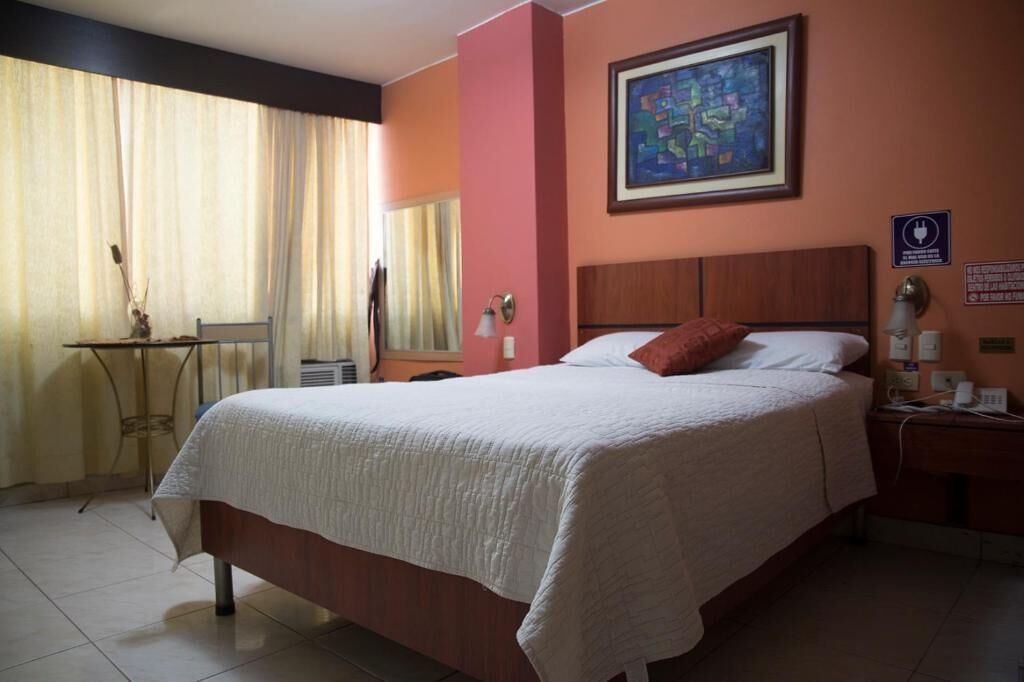 A hotel room with a bed, a desk, a chair, a mirror, and a painting on the wall.