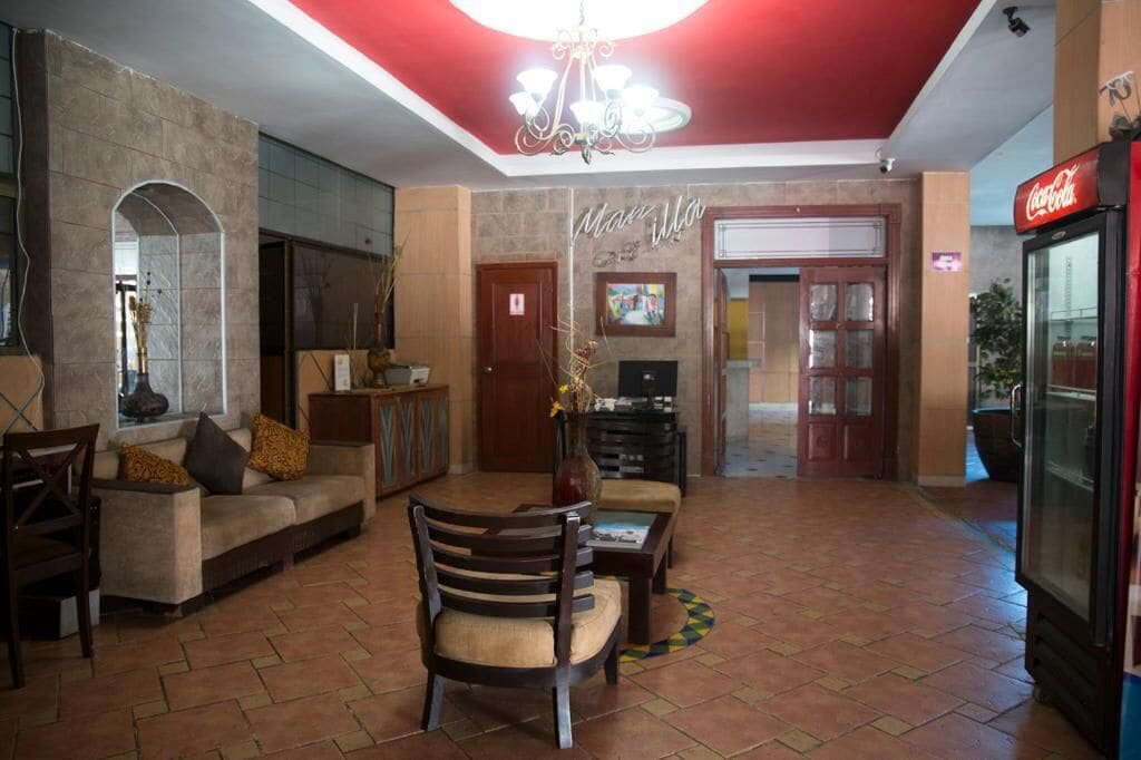 A spacious lobby with a red ceiling, a sofa, a wooden chair, a coffee table, and a Coca-Cola refrigerator.