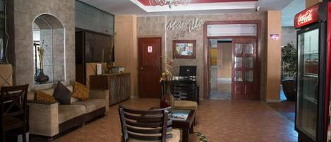 A spacious lobby with a red ceiling, a sofa, a wooden chair, a coffee table, and a Coca-Cola refrigerator.