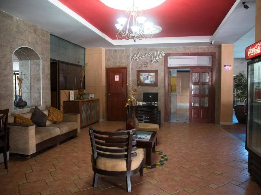 A spacious lobby with a red ceiling, a sofa, a wooden chair, a coffee table, and a Coca-Cola refrigerator.
