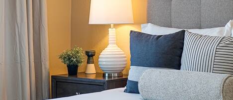 A hotel room with a bed, a nightstand, a lamp, a potted plant, and a painting on the wall.