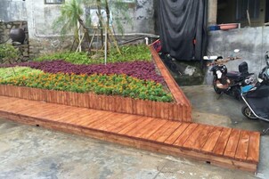Una terraza de madera con un jardín de flores, una motocicleta y una superficie de hormigón.